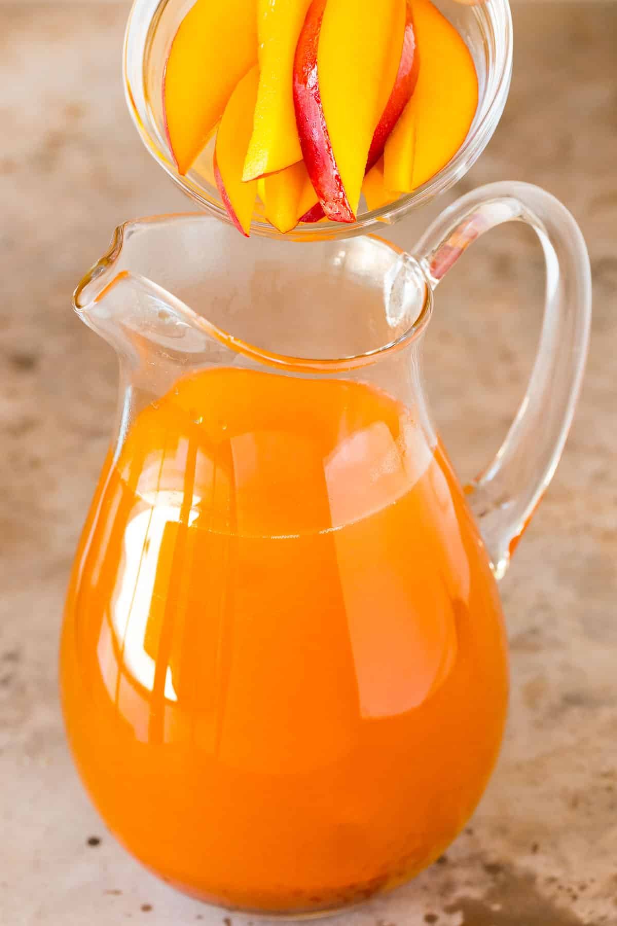 Mango slices being added to a pitcher of tea.