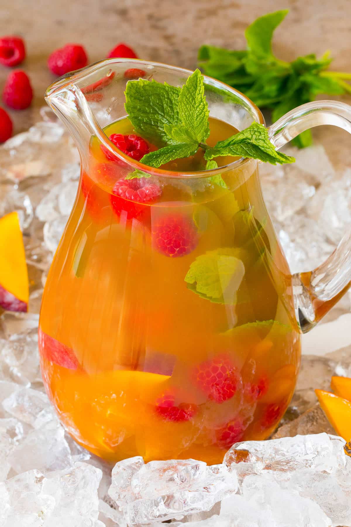 A pitcher of mango iced tea with raspberries and mint in it.