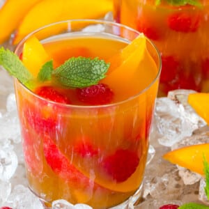 A glass of mango iced tea garnished with fresh fruit and mint.