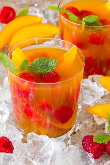 A glass of mango iced tea garnished with fresh fruit and mint.