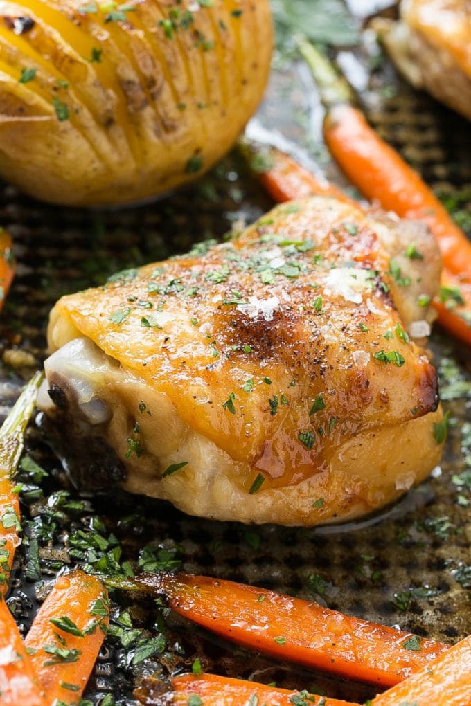 A roasted chicken thigh surrounded by carrots and potatoes.