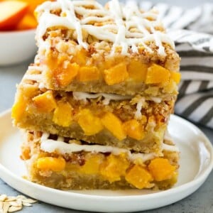 A stack of peach crumble bars topped with vanilla glaze.