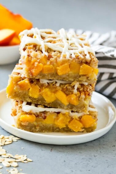 A stack of peach crumble bars topped with vanilla glaze.