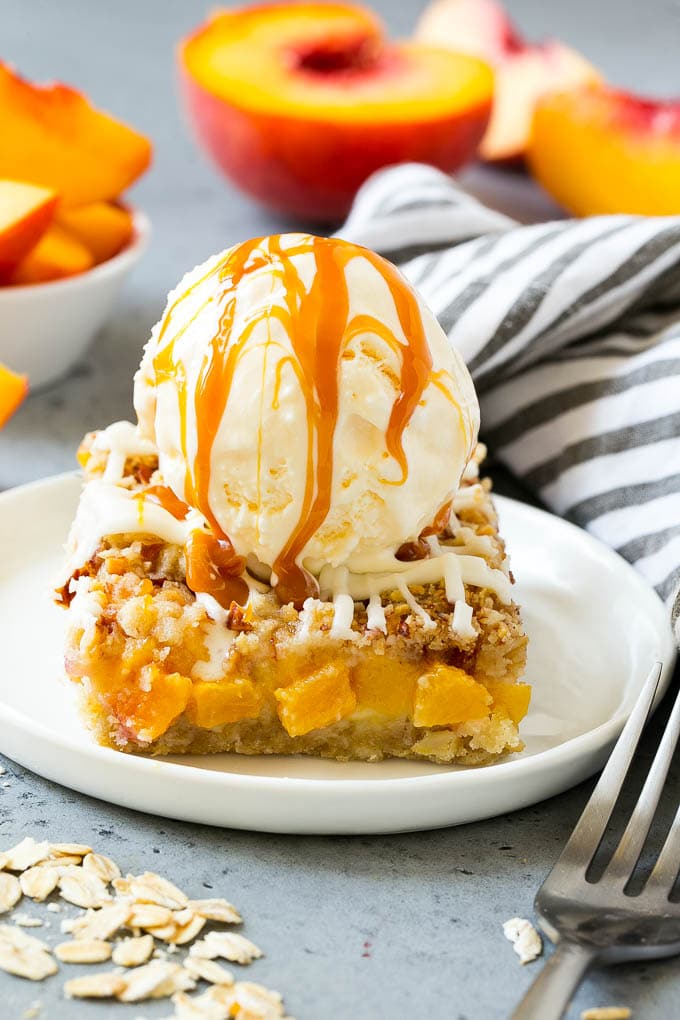 A peach crumble bar topped with a scoop of vanilla ice cream and salted caramel sauce.
