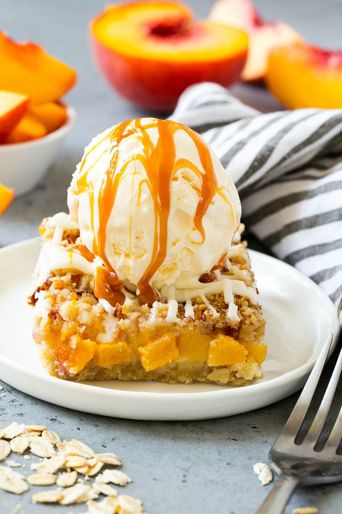 A peach crumble bar topped with a scoop of vanilla ice cream and salted caramel sauce.