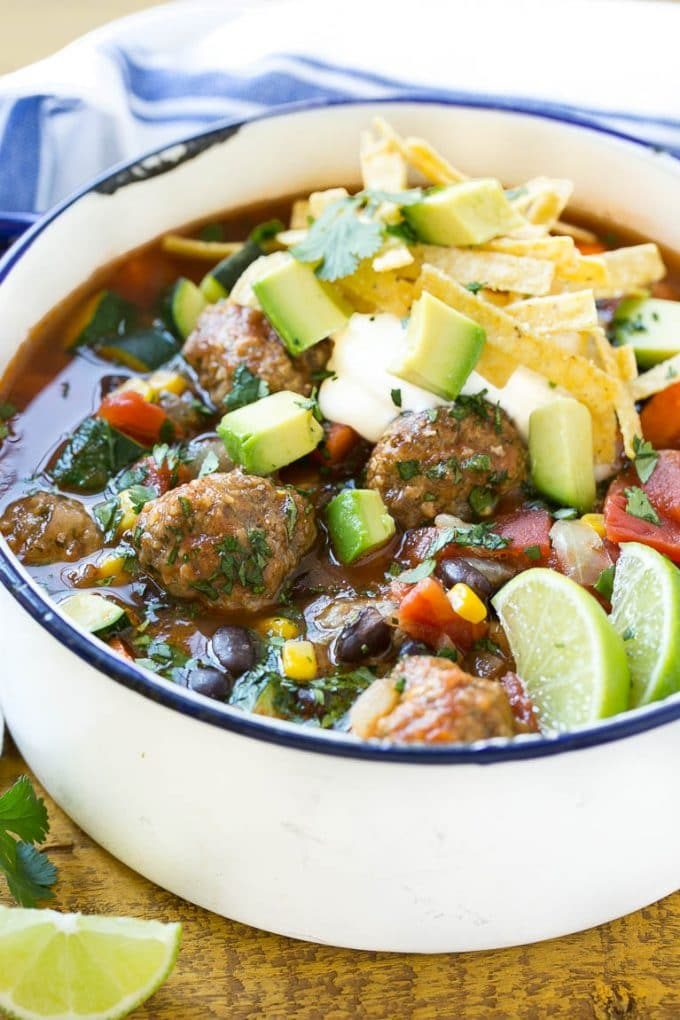 A pot of meatball soup with corn, beans and carrots, topped with sour cream and avocado.