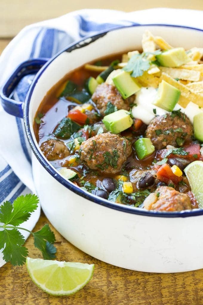 A pot of Mexican meatball soup topped with sour cream, tortilla strips and avocado.