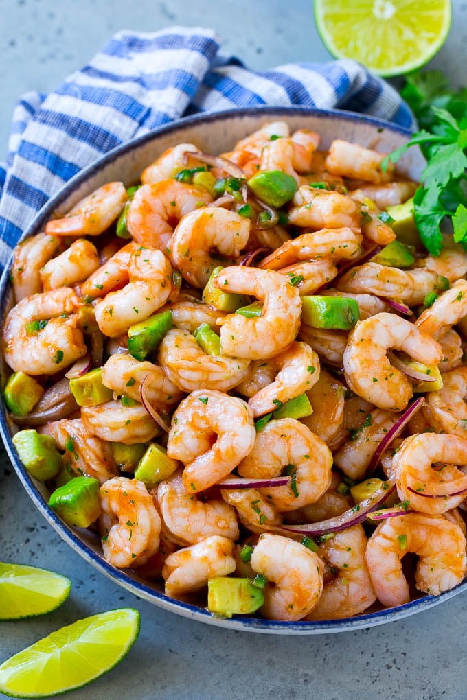 A bowl of Mexican shrimp cocktail with red onion, avocado, homemade sauce and cilantro.
