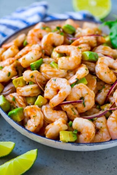 A serving bowl of Mexican shrimp cocktail which contains small shrimp, diced avocado, herbs and jalapeno.