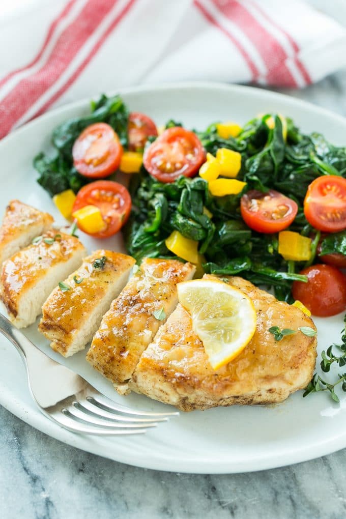 A plate of sliced pan seared chicken breast served with spinach and vegetables.