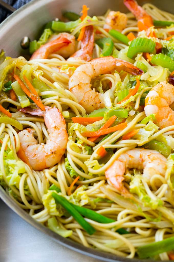 Shrimp nestled in a pan of chow mein noodles with colorful vegetables.