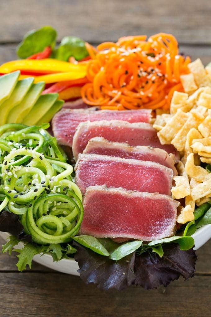 A bowl of ahi tuna salad with thinly sliced seared tuna and an assortment of colorful veggies.