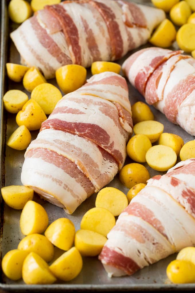 Bacon wrapped chicken with potatoes on a sheet pan.