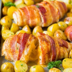 Bacon wrapped stuffed chicken breast on a sheet pan with roasted potatoes.