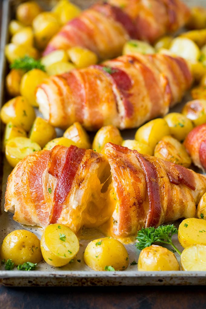 Bacon wrapped stuffed chicken breast on a sheet pan with roasted potatoes.