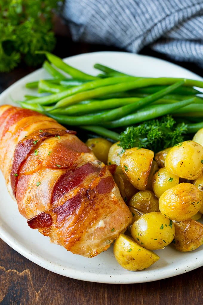 A plate with bacon wrapped stuffed chicken breast, roasted potatoes and green beans.