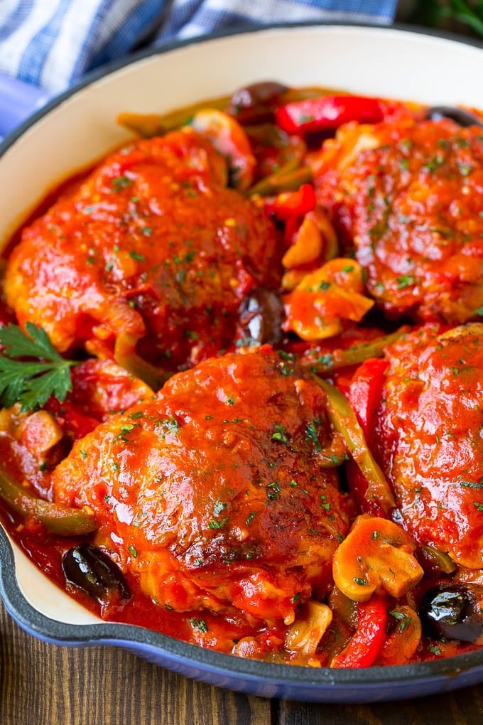 Chicken cacciatore in a skillet with tomato sauce, peppers and mushrooms.