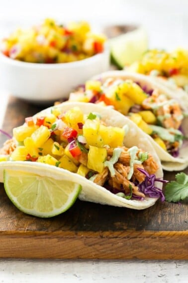 This recipe for pulled chicken tacos with pineapple salsa is flavorful shredded chicken combined topped with sweet and tangy salsa and creamy cilantro sauce, all stuffed inside warm corn tortillas.