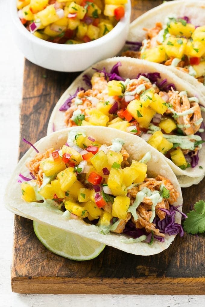 This recipe for pulled chicken tacos with pineapple salsa is flavorful shredded chicken combined topped with sweet and tangy salsa and creamy cilantro sauce, all stuffed inside warm corn tortillas.