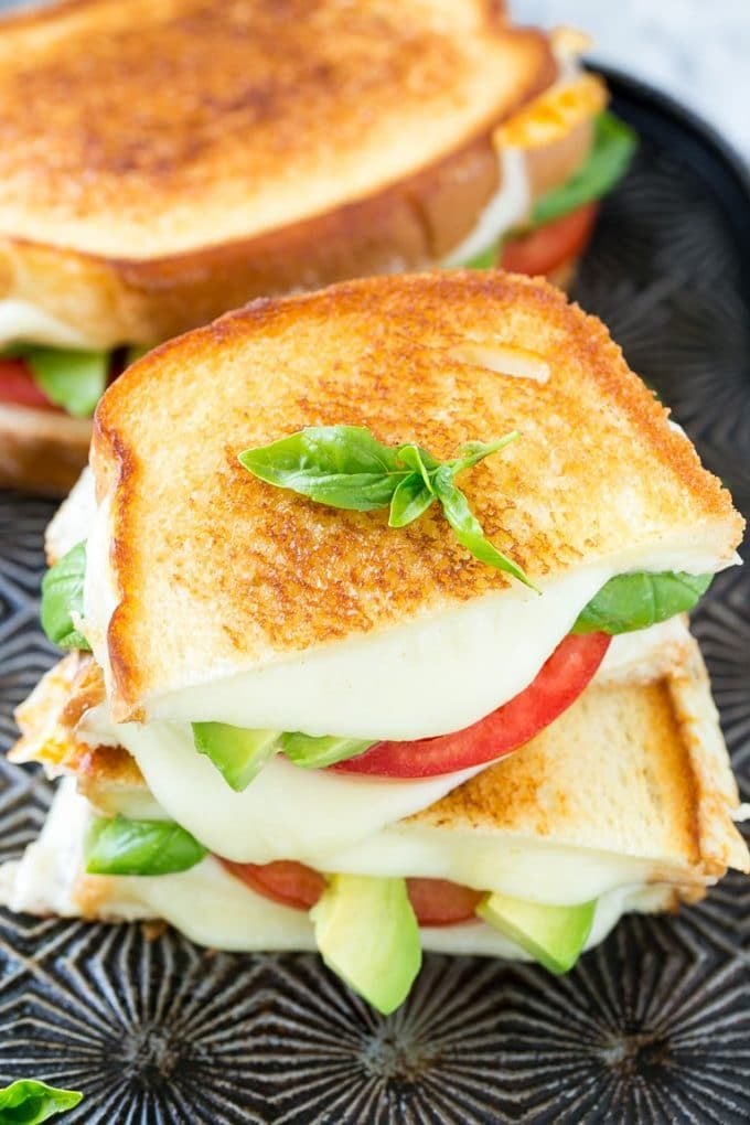 A grilled caprese sandwich with tomato slices, melted cheese and avocado.