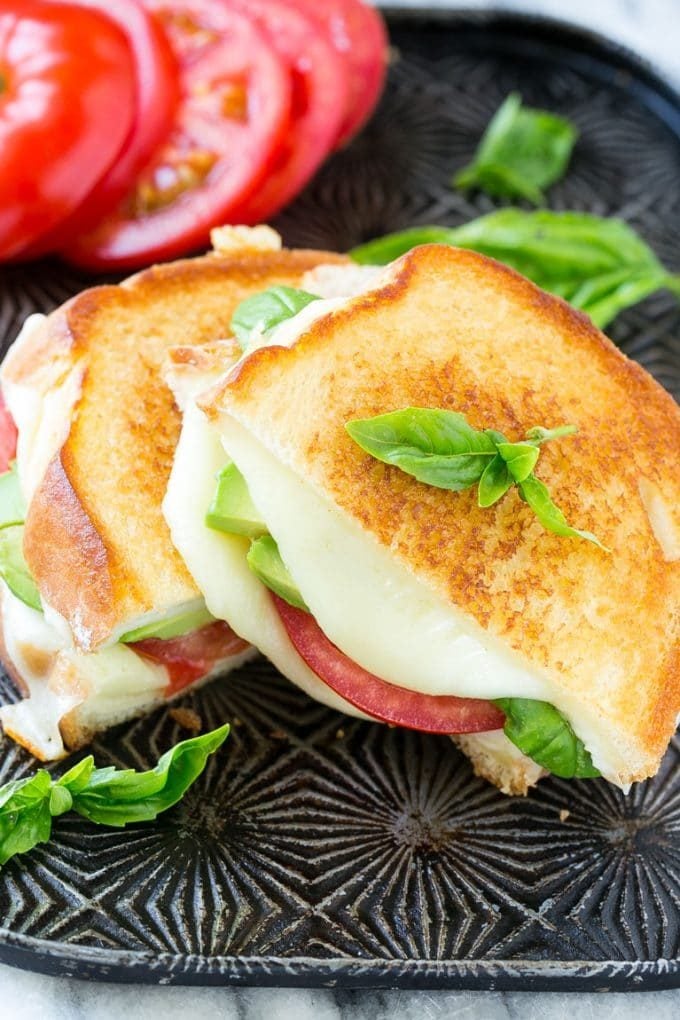 Caprese sandwich with melted mozzarella cheese, fresh tomatoes, sliced avocado and basil leaves.