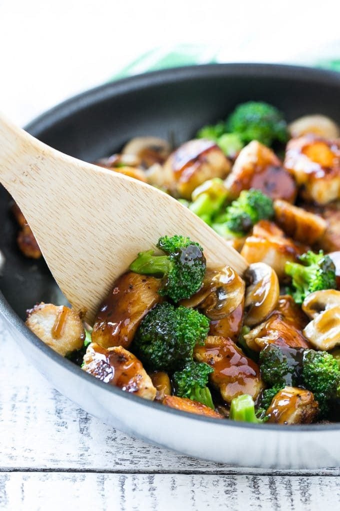 A spatula scooping chicken and broccoli stir fry out of a pan.