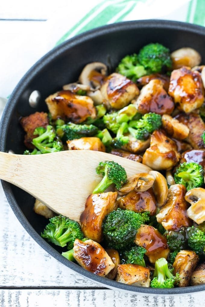 A stir fry of chicken, broccoli and mushrooms in a skillet with a spatula.