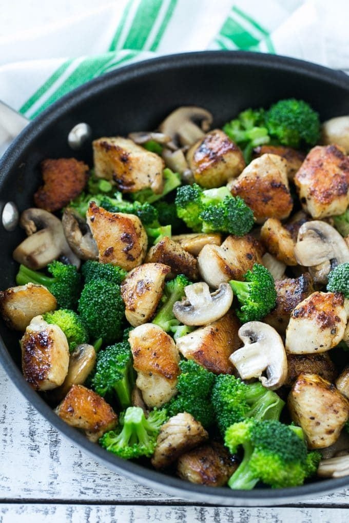 Sauteed chicken pieces, broccoli florets and mushrooms in a pan.
