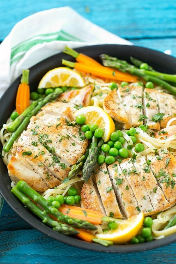 A pan of chicken primavera pasta with chicken breast, lemon sauce, peas, carrots and asparagus.