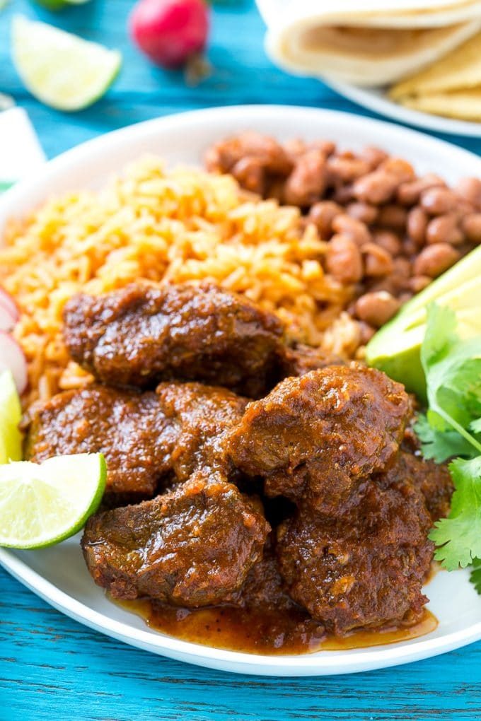 Chile colorado on a plate served with rice and beans.