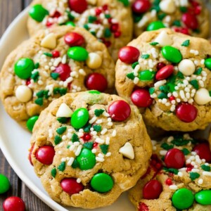 A plate of Christmas monster cookies which are decorated with M&M's, white chocolate and sprinkles.