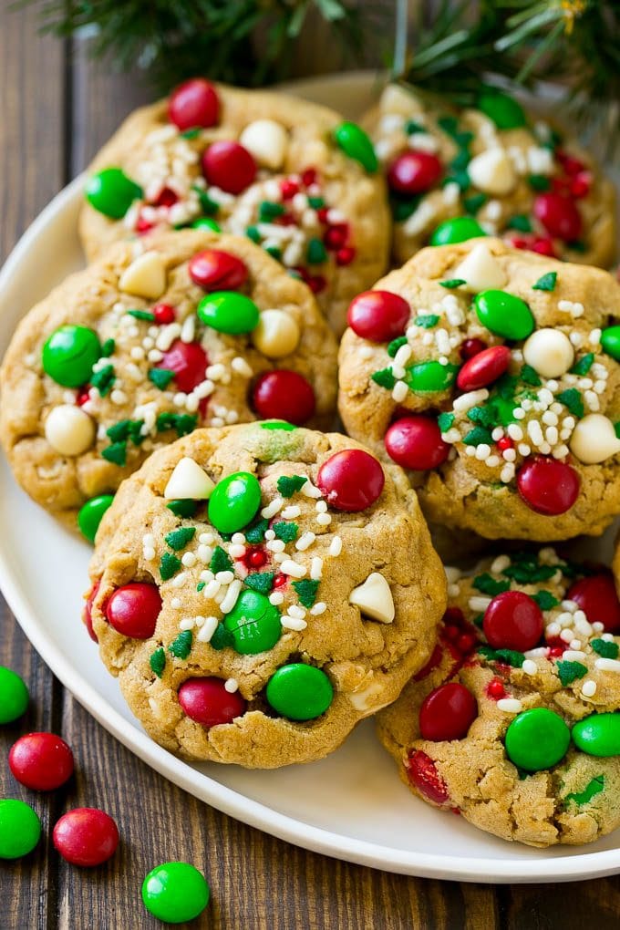 A plate of Christmas monster cookies which are decorated with M&M's, white chocolate and sprinkles.