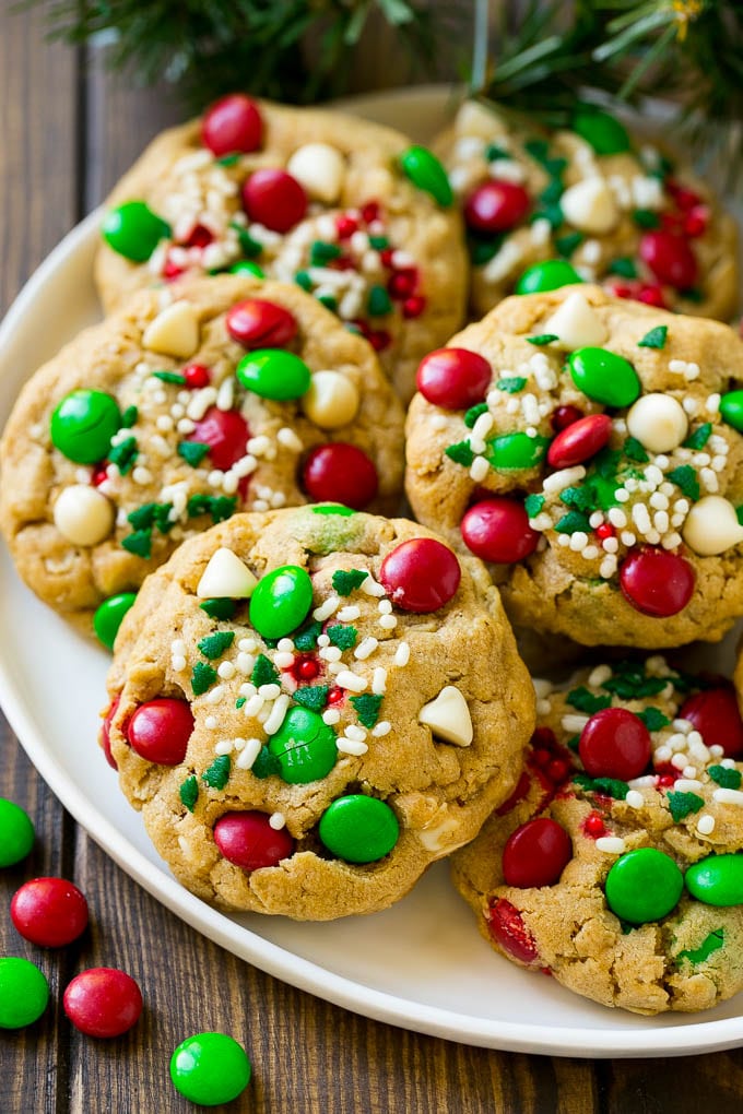 A plate of Christmas monster cookies which are decorated with M&M's, white chocolate and sprinkles.