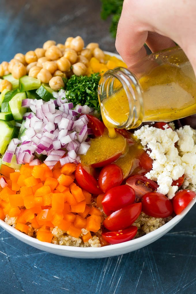 Dressing being poured over a bowl of vegetables and quinoa.