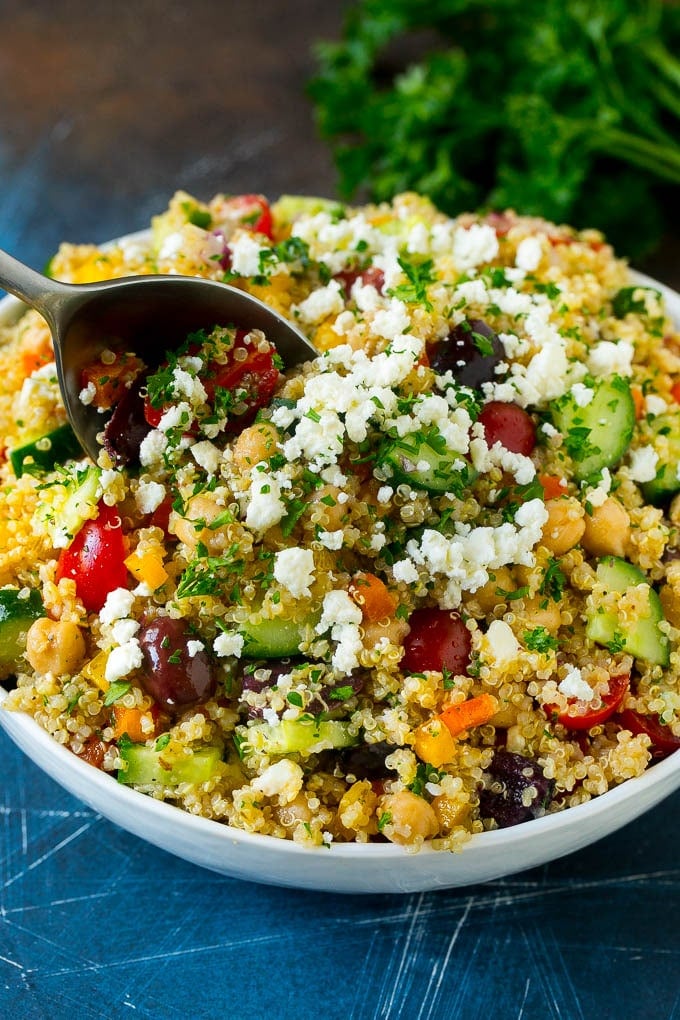 A serving spoon in a bowl of quinoa salad with feta and vegetables.