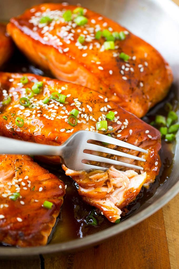 A fillet of teriyaki salmon with a fork cutting into it.