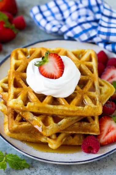 A stack of buttermilk waffles topped with syrup, whipped cream and fresh fruit.