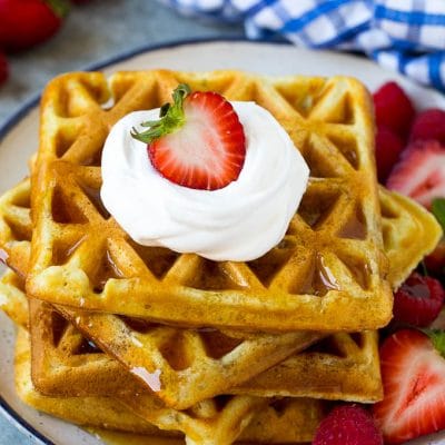 A stack of buttermilk waffles topped with syrup, whipped cream and fresh fruit.