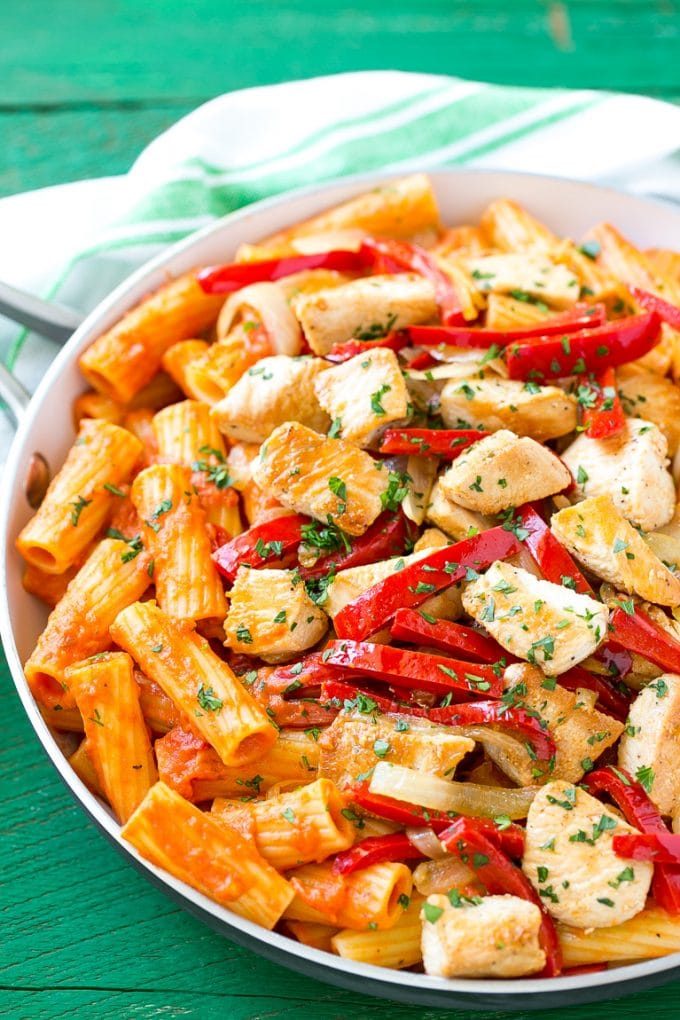 A skillet of chicken riggies topped with bell peppers, sliced onion and chopped parsley.