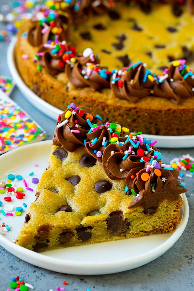 A slice of cookie cake topped with a layer of chocolate frosting and colorful sprinkles.