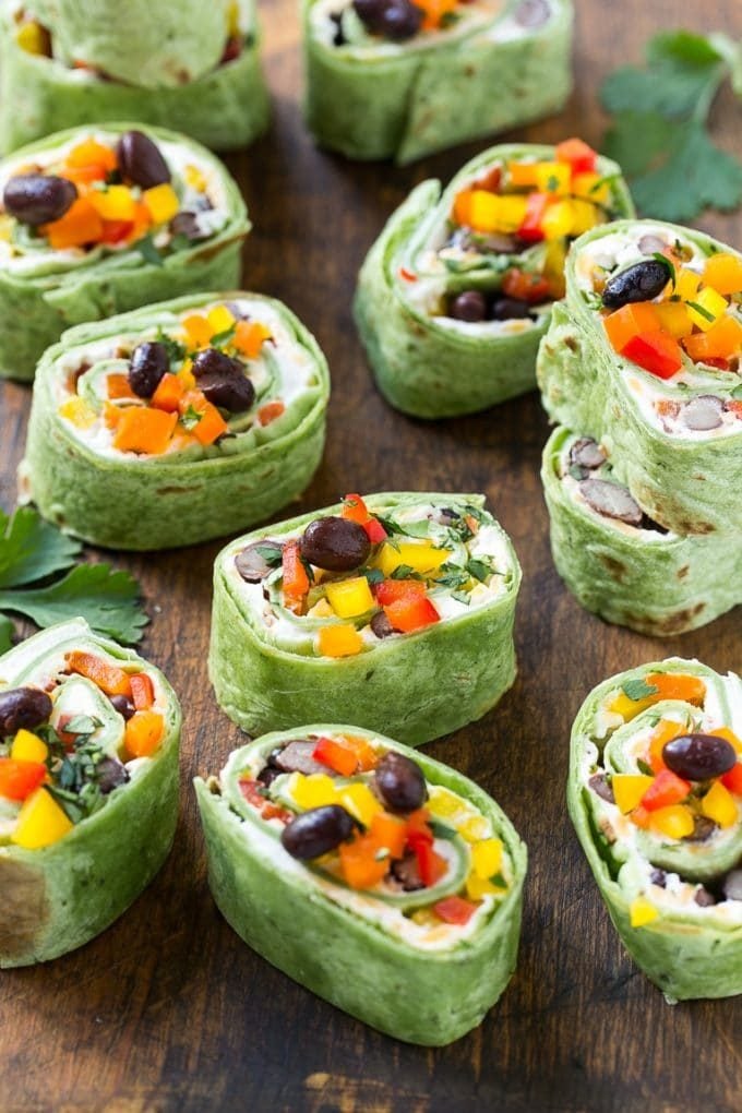 A board full of Mexican tortilla pinwheels garnished with peppers and black beans.