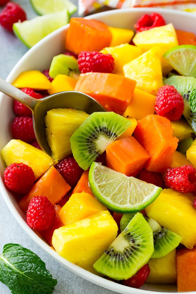 A bowl of tropical fruit salad with a serving spoon.