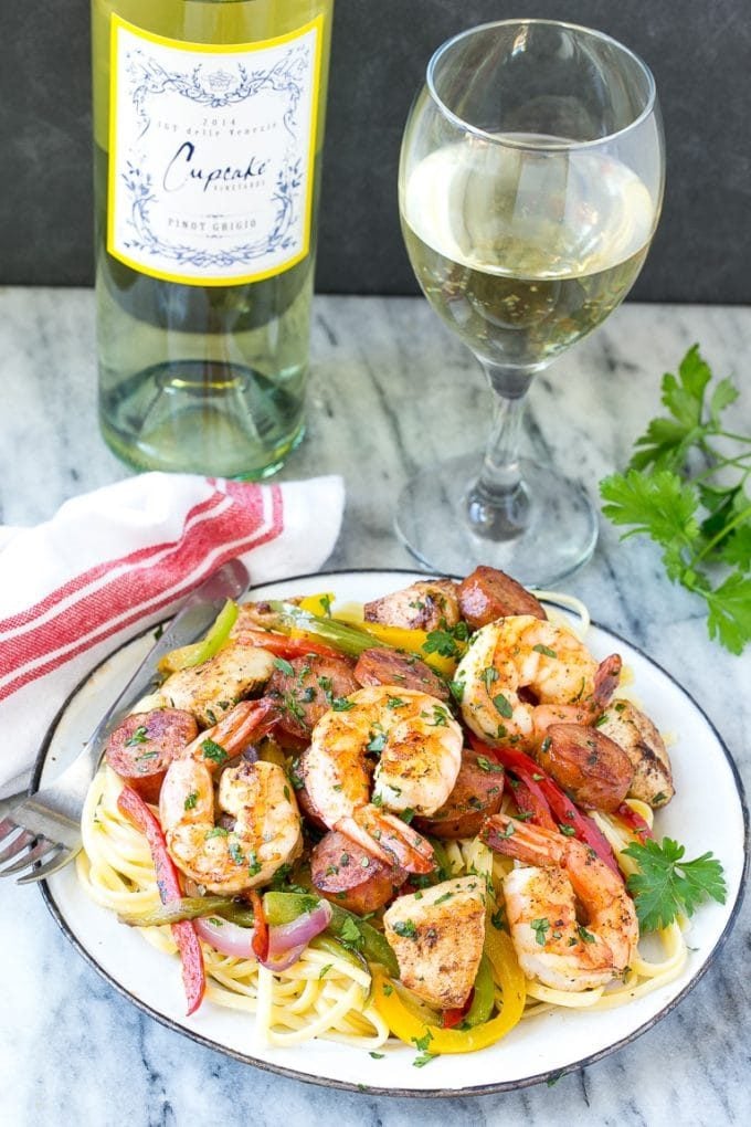 A plate of jambalaya pasta served with a glass of white wine.