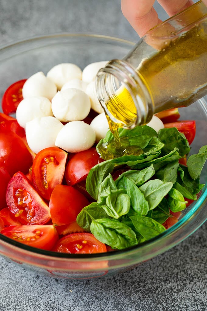 Olive oil being poured over tomatoes, mozzarella and basil leaves.