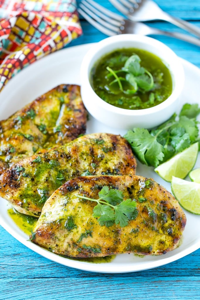 A serving plate of cilantro lime chicken breasts garnished with fresh cilantro leaves and lime wedges.