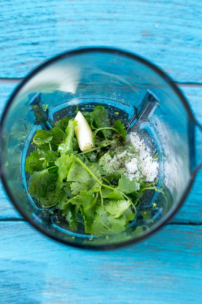 A blender full of cilantro leaves, garlic, lime juice and olive oil.