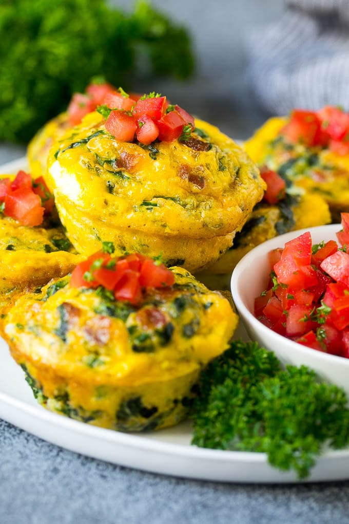 Egg muffins on a serving plate topped with diced tomatoes.