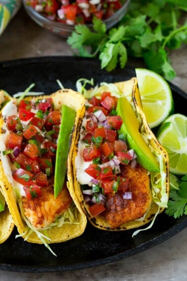 Fish tacos wrapped in corn tortillas with sliced avocado and pico de gallo.