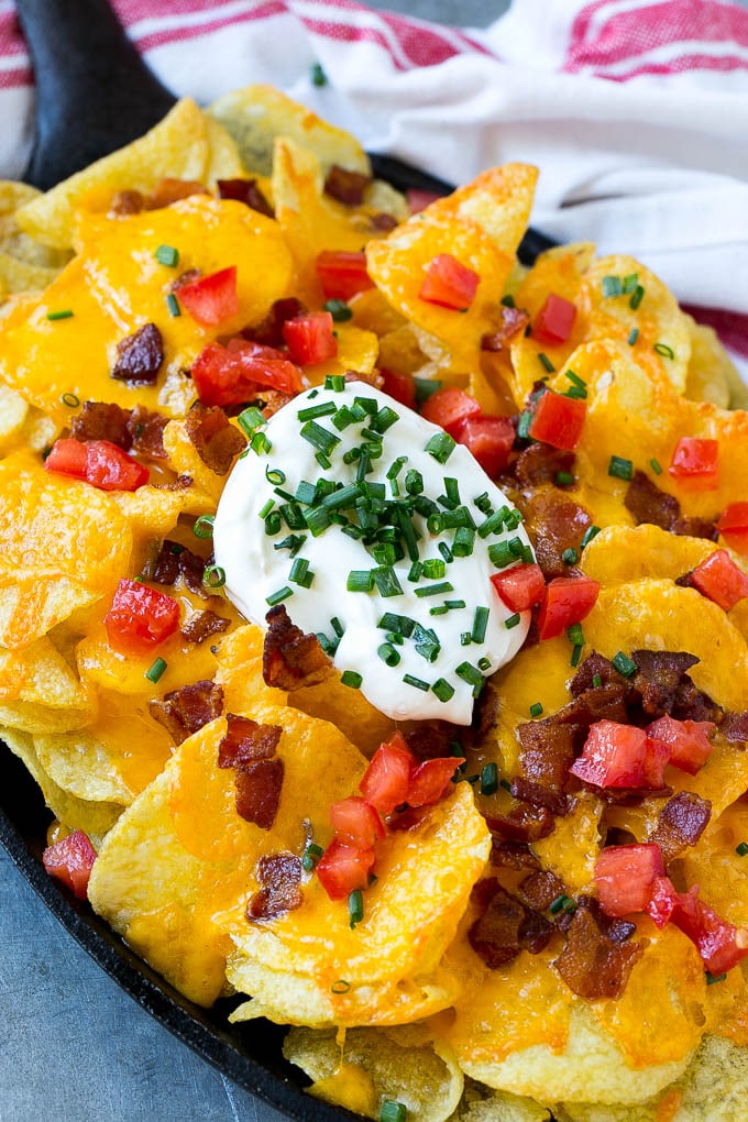 A skillet of Irish nachos topped with melted cheese, bacon, tomatoes and sour cream.