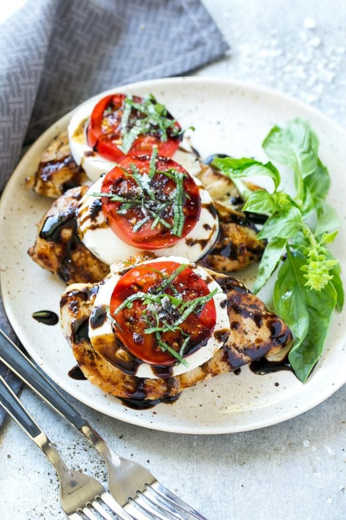A plate of caprese chicken breasts topped with cheese, tomatoes and basil.